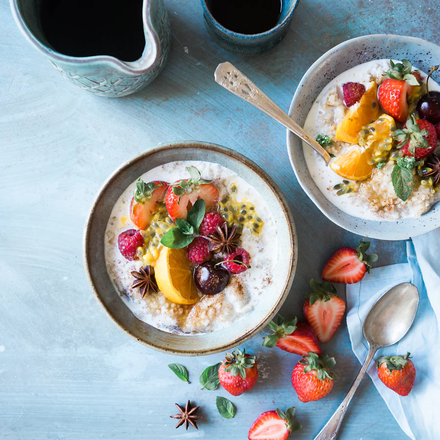 Two bowls of porridge topped with strawberries, orange and passion fruit